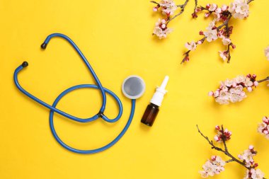 Stetoskop ve burun spreyi ile sarı arka planda güzel çiçek açan dallar. İlkbahar konsepti. Düz yatış, üst görünüm