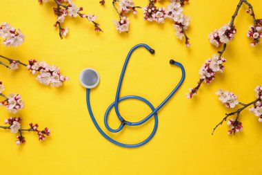 Sarı arka planda güzel çiçekli dalları olan steteskop. İlkbahar konsepti. Düz yatış, üst görünüm