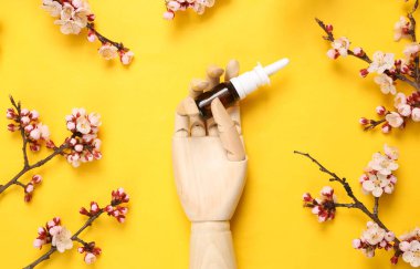 Burun spreyi tutan ahşap el sarı arka planda güzel çiçekli dallar..