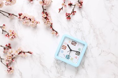 Mermer zemin üzerinde güzel pembe çiçekli dalları olan çalar saat. İlkbahar konsepti. Düz yatış, üst görünüm