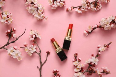 Kırmızı ruj ve pembe arka planda güzel çiçekli dallar. İlkbahar, güzellik konsepti. Düz yatış, üst görünüm.