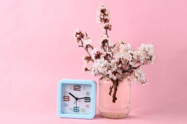 Alarm saati ve pembe arka planda cam kavanozdaki güzel çiçek dalları.