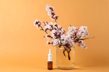 Burun spreyi ve turuncu arka planda cam kavanozda çiçek açan güzel dallar..