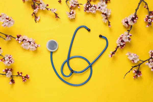 Sarı arka planda güzel çiçekli dalları olan steteskop. İlkbahar konsepti. Düz yatış, üst görünüm
