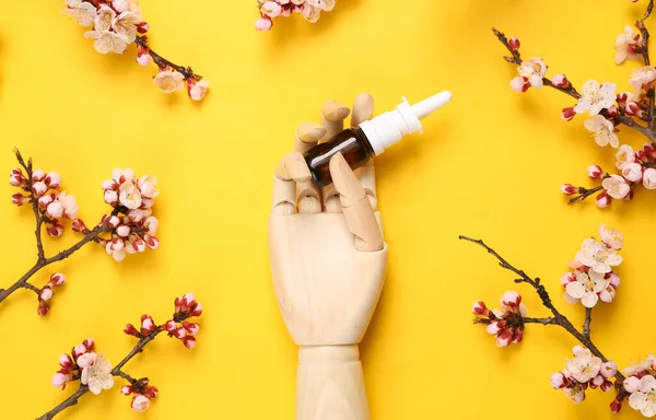 Burun spreyi tutan ahşap el sarı arka planda güzel çiçekli dallar..