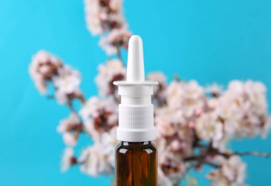 Burun spreyi ve mavi arka planda güzel çiçekli dallar..