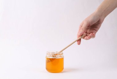 Beyaz arka planda bal kavanozu ile bal kaşığı tutan eller.