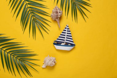 Deniz kabukları, yelkenli, sarı arka planda palmiye yeşili yapraklar. Seyahat konsepti. Tropikal kompozisyon. Üst Manzara. Düz yatıyordu