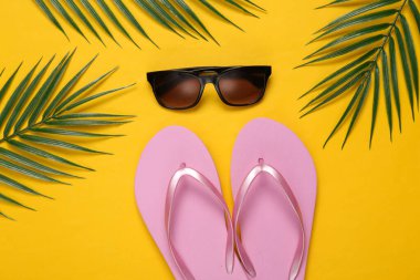 Parmak arası terlikler, güneş gözlüğü, sarı arka planda palmiye yeşili yapraklar. Seyahat konsepti. Tropikal kompozisyon. Üst Manzara. Düz yatıyordu