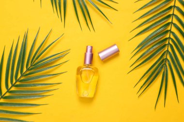 Sarı arka planda parfüm şişesi ve palmiye yaprakları. Tropikal, güzellik kompozisyonu. Üst Manzara. Düz yatıyordu