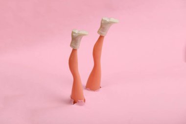 Pembe kağıttaki yırtık bir delikten ayakkabılar içinde bebek ayakları. Minimalizm, kavram sanatı