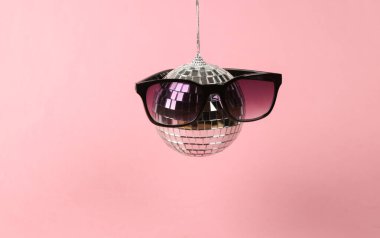 Pembe arka planda güneş gözlüklü disko topu. Minimalizm partisi konsepti