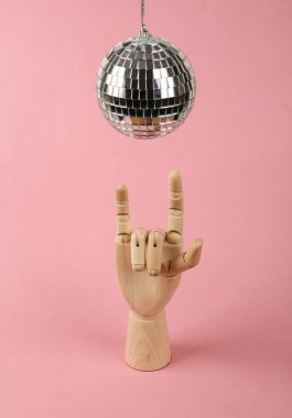 Disko topu ve ahşap el, pembe arka planda rock hareketi gösteriyor. Minimalizm partisi konsepti