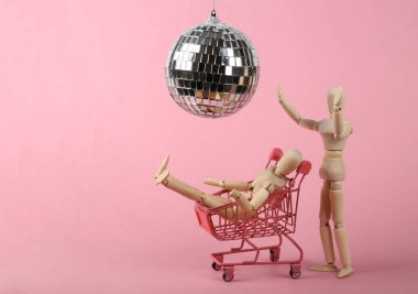 Alışveriş arabasında, disko topunun altında pembe arka planda iki kukla. Minimalizm partisi konsepti