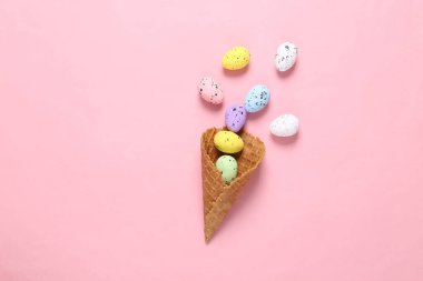 Pembe arka planda waffle külahında renkli yumurtalar. Yaratıcı Paskalya düzeni
