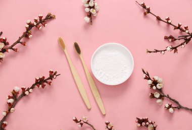 Eko bambu diş fırçaları, diş fırçası ve pembe arka planda güzel beyaz çiçekli dallar. İlkbahar, eko konsepti. Düz yatış, üst görünüm.