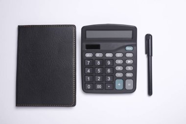 Beyaz arka planda not defteri olan bir hesap makinesi. Düz yatıyordu