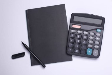 Beyaz arka planda not defteri olan bir hesap makinesi. Düz yatıyordu