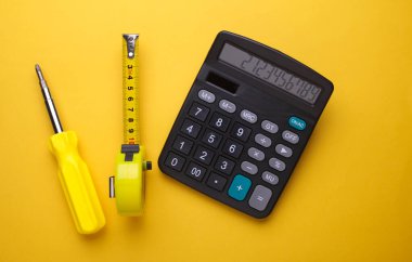 Sarı zemin üzerinde şerit ölçü ve tornavida bulunan hesap makinesi