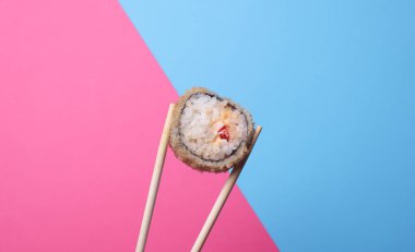 Çin yemek çubuklarında pembe mavi arka planda suşi rulosu var.