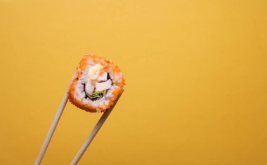 Çin yemek çubuklarında sarı arka planda suşi rulosu var.