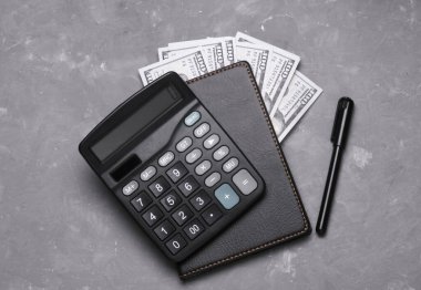 Defterli hesap makinesi, gri beton arka planda 100 dolarlık banknotlar.