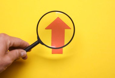 Bir büyüteçle el, sarı zemin üzerinde kırmızı büyüme okunu inceler