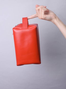 Gri arka planda kırmızı deri kozmetik çanta düzenleyicisi tutan bir kadın.