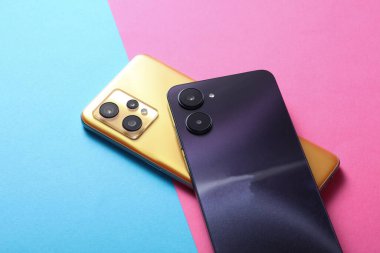The back side of two modern smartphones with a dual cameras on pink blue background