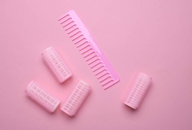 Plastik bigudiler ve pembe arka planda saç tarağı. Düz yatıyordu