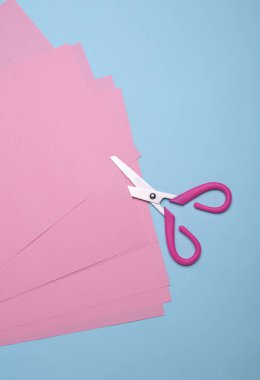 Çocukların yaratıcılığı ve makasları için mavi arka planda pembe kağıtlar.