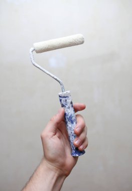 Duvara karşı inşaat rulosu tutan bir erkek el.