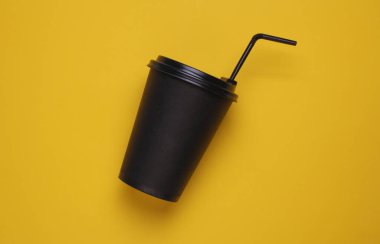 Sarı arka planda saman ve kapaklı sıcak içecekler için siyah tek kullanımlık bardak.