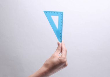 Gri arka planda üçgen bir cetvel tutuyor.