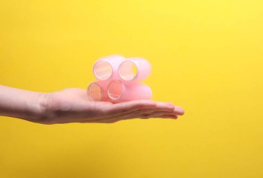 Sarı arka planda plastik bigudiler tutan kadın.