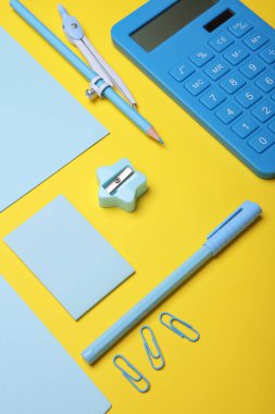 Sarı arka planda mavi kırtasiye seti. Okula, eğitime, ofis malzemelerine. Düz yatıyordu. Üst Manzara. Yaratıcı yerleşim