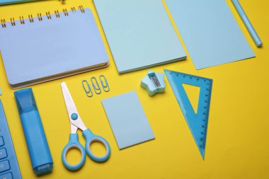 Sarı arka planda mavi kırtasiye seti. Okula, eğitime, ofis malzemelerine. Düz yatıyordu. Üst Manzara. Yaratıcı yerleşim