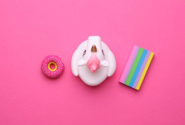 Pembe arka planda donut ve gökkuşağı olan lastik banyo tek boynuzlu atı. Üst görünüm.