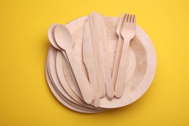 Sarı arka planda bir dizi ahşap eko çanak. Tabaklar, çatallar, bıçaklar ve kaşıklar
