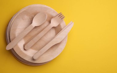 Sarı arka planda bir dizi ahşap eko çanak. Tabaklar, çatallar, bıçaklar ve kaşıklar