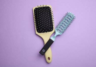 İki saç fırçası, mor arka planda plastik taraklar.