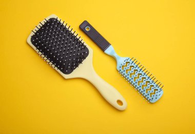İki saç fırçası, sarı arka planda plastik tarak.