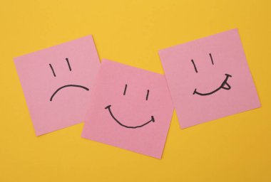 Kare kağıtlarda mutlu ve mutsuz yüzler, sarı arka plan. İş konsepti