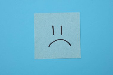 Kare not kağıdındaki mutsuz surat, mavi arkaplan. İş konsepti