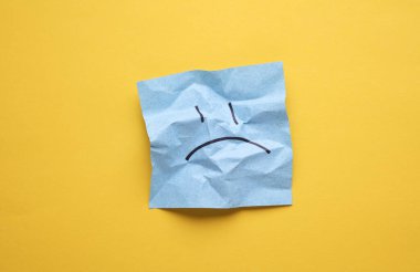 Buruşuk kareli not kağıdındaki mutsuz surat, sarı arka plan. İş konsepti