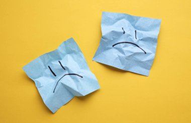 Buruşuk karton kağıtlarda mutsuz yüzler, sarı arka plan. İş konsepti