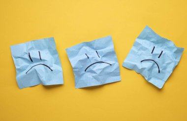 Buruşuk karton kağıtlarda mutsuz yüzler, sarı arka plan. İş konsepti