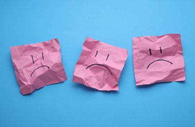 Buruşuk karton kağıtlarda mutsuz yüzler, mavi arka plan. İş konsepti