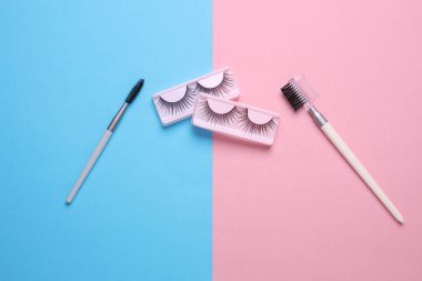 False eyelashes and makeup brushes on blue pink background