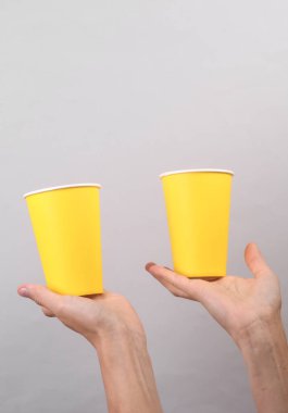 Gri arka planda tek kullanımlık sarı karton bardakları tutan kadın.